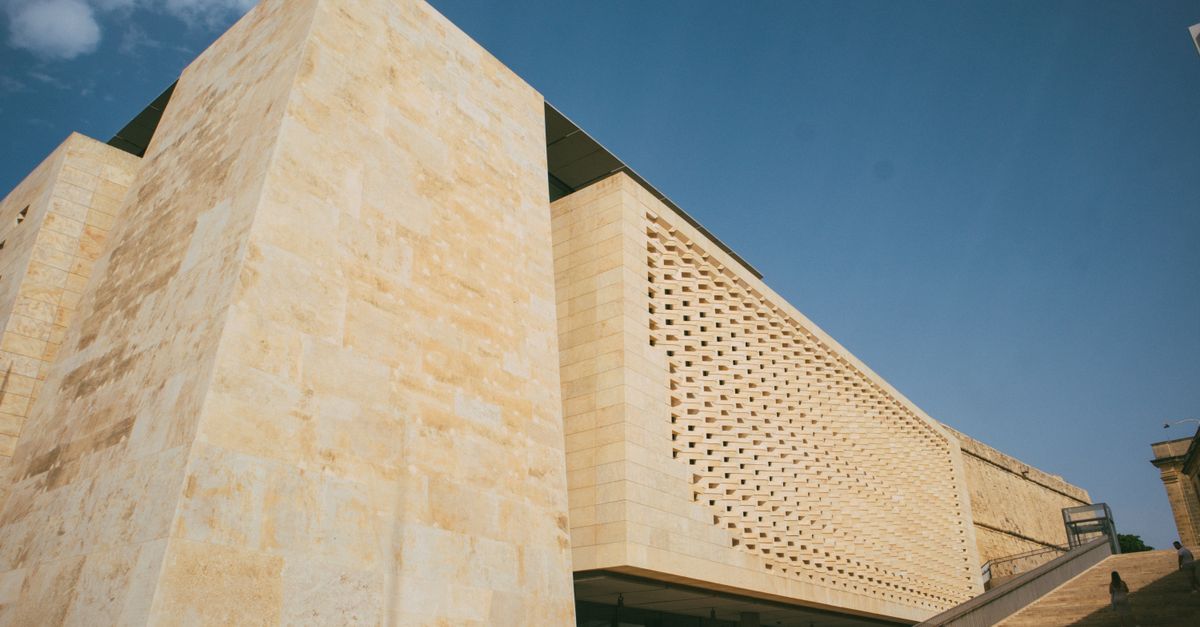 Low angle shot of a modern building with beige stone facade against a clear blue sky.