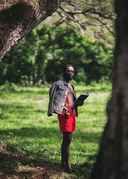 A man reading a book outdoors in Cape Coast, Ghana, wearing sunglasses and a denim jacket.