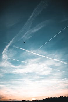 A paraglider soars beneath the vibrant twilight sky with jet contrails in Genève.