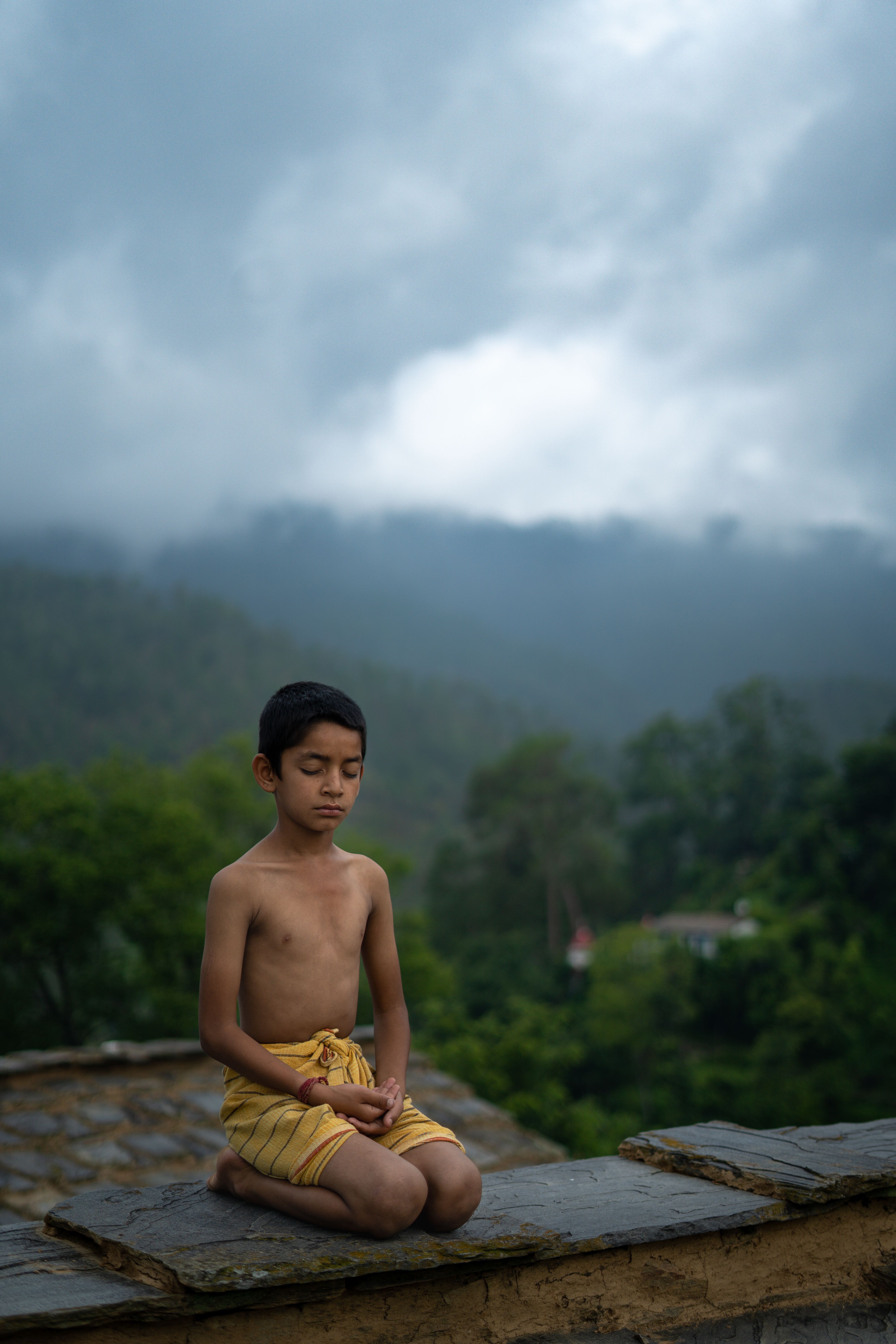 A young boy practices meditation outside on a foggy day, surrounded by lush greenery.