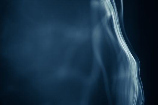 Ethereal wisps of smoke create intricate patterns against a blue backdrop, evoking a sense of mystery and fluidity.
