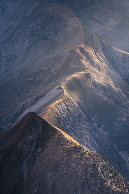 Stunning aerial view of a rugged mountain range captured during golden hour with dramatic sunlight.