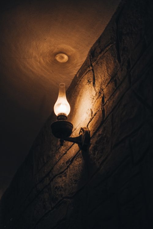 Free A vintage oil lamp casts warm light on a rustic stone wall indoors. Stock Photo