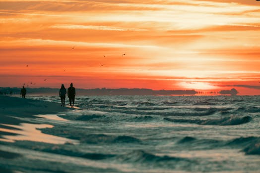 A vibrant sunset over the ocean with silhouettes walking along the beach, creating a peaceful scene.