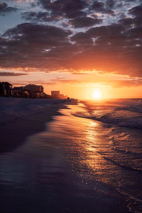 Free Vibrant sunset on a beach with waves gently lapping the shore, creating a serene and picturesque scene. Stock Photo