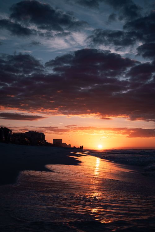 Free A breathtaking sunset with waves gently crashing on a peaceful beach, casting warm reflections. Stock Photo