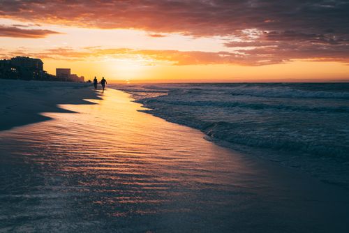 Free Two people walk along a serene beach at sunset, with waves gently crashing on the shore. Stock Photo