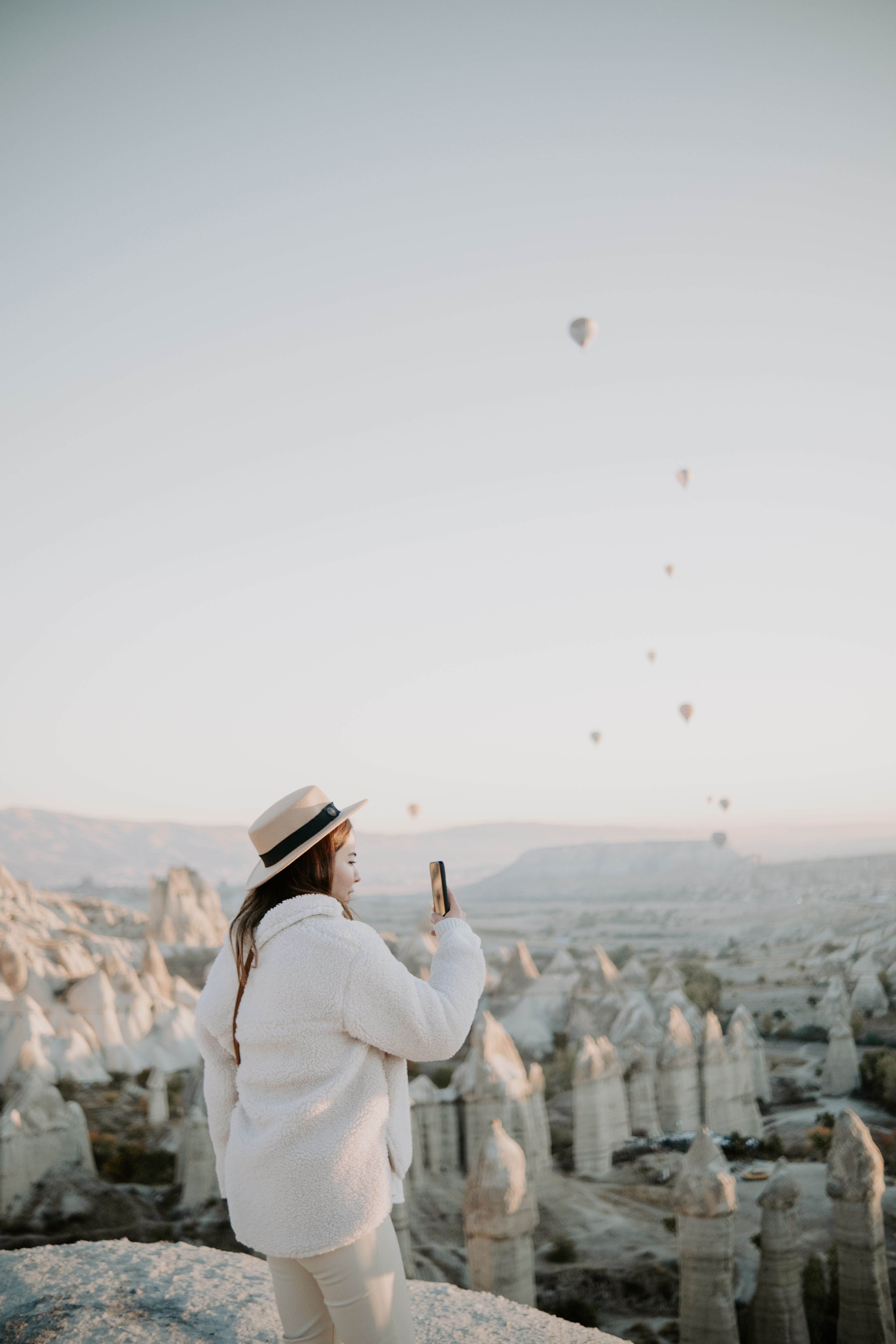 Woman capturing hot air balloons over Cappadocia landscape at sunrise.