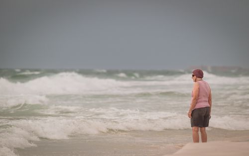 Free A woman in casual attire looks out at the ocean on a cloudy day, absorbed in thought. Stock Photo
