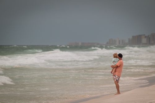 Free A father holds his child at the beach, gazing at the sea under a cloudy sky. Stock Photo
