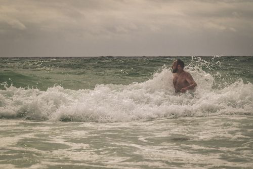 Free A man enjoying a refreshing dip in the sea waves under a cloudy sky. Stock Photo