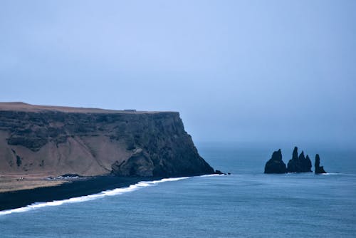 Brown Rock Formation on Sea Under Foggy Sky