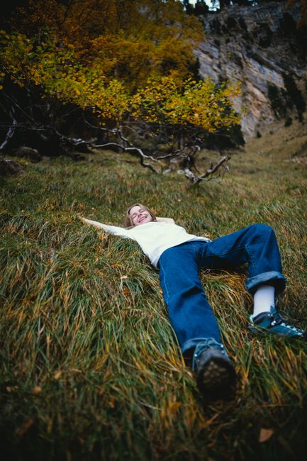 A young girl enjoys a moment of relaxation lying on grass amidst a scenic mountain backdrop.