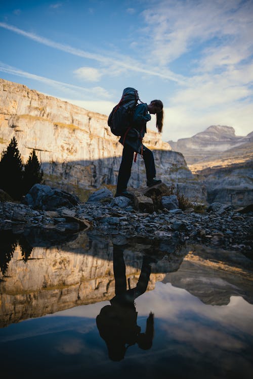 Woman in Denim Jacket Walking on Gray Rocks near River