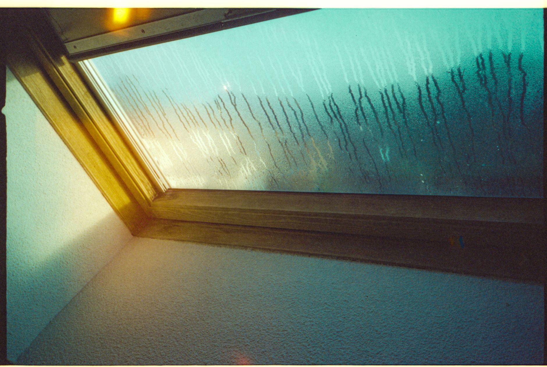 A view through a skylight window with raindrops and a misty, moody atmosphere.
