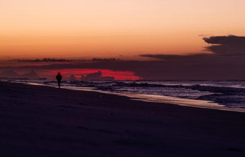 Free A person walks along the beach with a vibrant sunset sky reflecting on the ocean waves. Stock Photo
