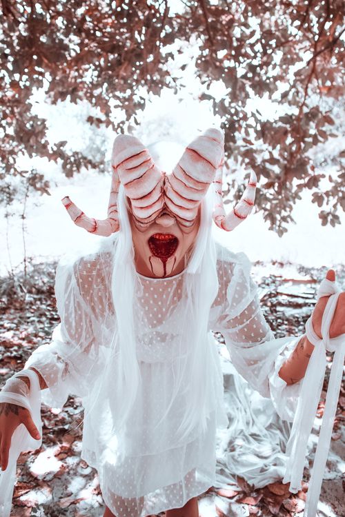 Free A woman in artistic horror makeup with horns and blood in a surreal outdoor setting. Stock Photo