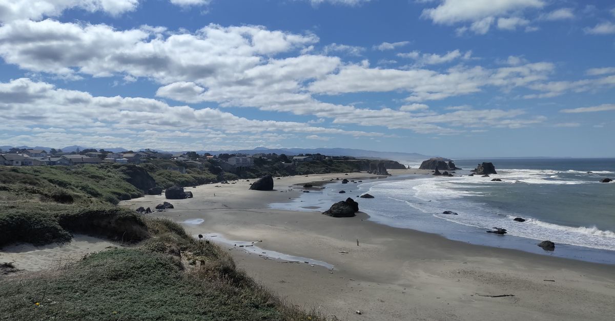 Wide view of a serene beach with scattered rocks under a partly cloudy sky.