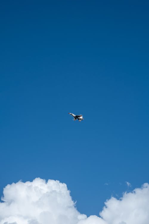Free High-altitude fighter jet captured midair with clear blue sky and clouds. Stock Photo