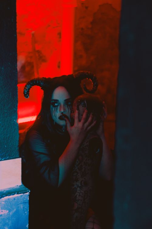 Free A woman in eerie costume with horns holding a mask in a dimly lit setting. Stock Photo