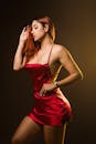 一位穿着红色连衣裙的时尚红发女郎在黑暗的背景下优雅地摆姿势