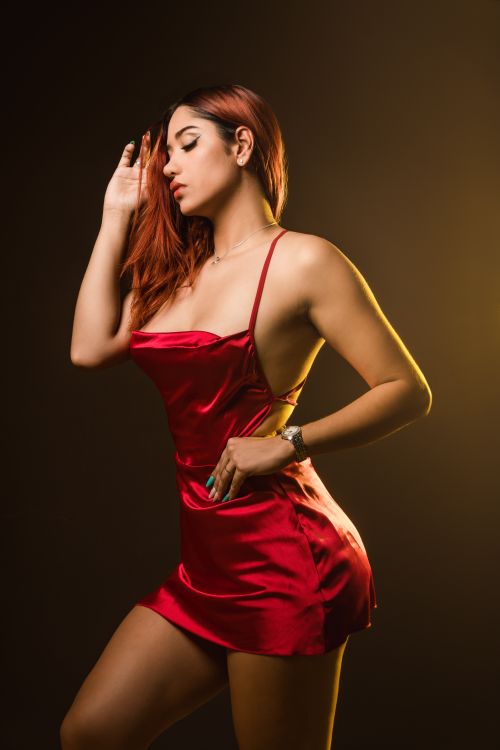 Free A fashionable redhead in a red dress posing gracefully against a dark background. Stock Photo