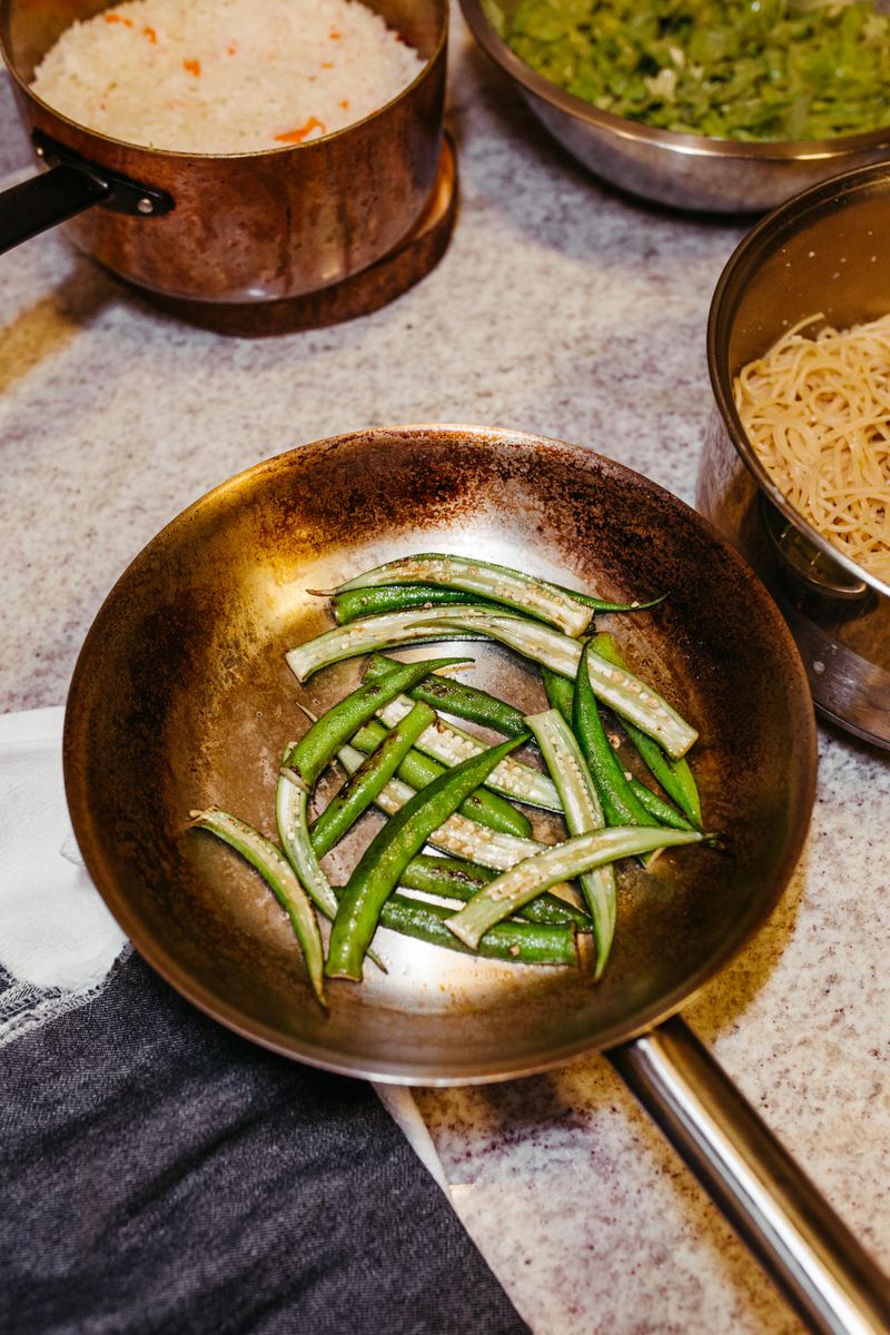 Okra Plant Guide: Growing, Harvesting, and Using This Vegetable Fresh okra sizzling in a copper pan, accompanied by rice and pasta ingredients