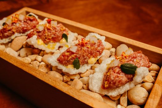 Delicious beef tartare served on crispy rice crackers with seasoning, offering a gourmet dining experience.