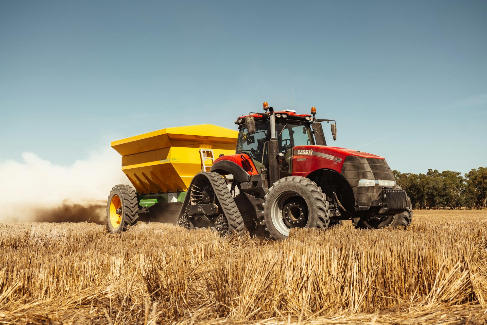 Red tractor pulling yellow trailer in a sunny rural field during harvesting season.