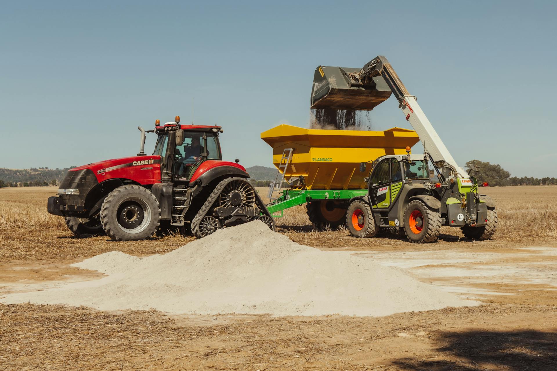 A tractor and loader work together to spread fertilizer on a farm field.