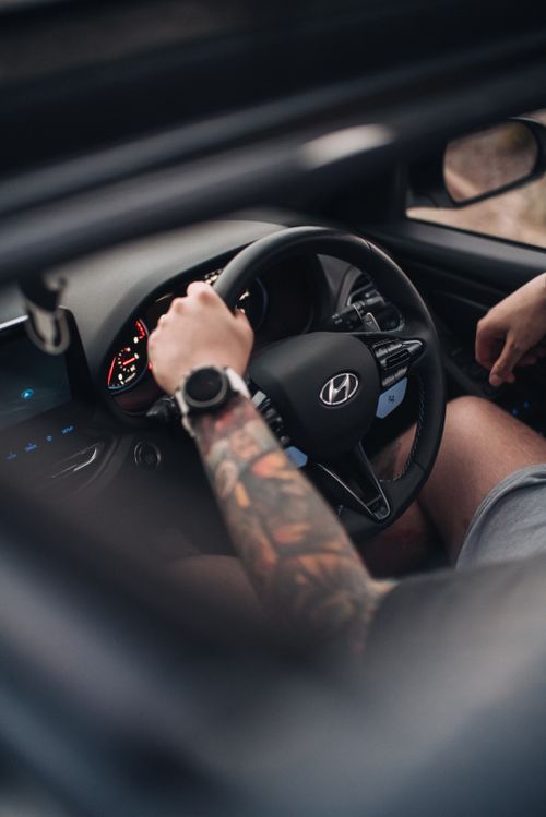 Free Close-up of tattooed arm holding Hyundai steering wheel inside a car, showcasing driving details. Stock Photo