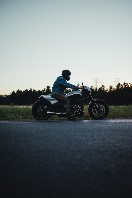 Free A motorcyclist sits on a motorcycle along a rural road at dusk, showcasing adventure and freedom. Stock Photo