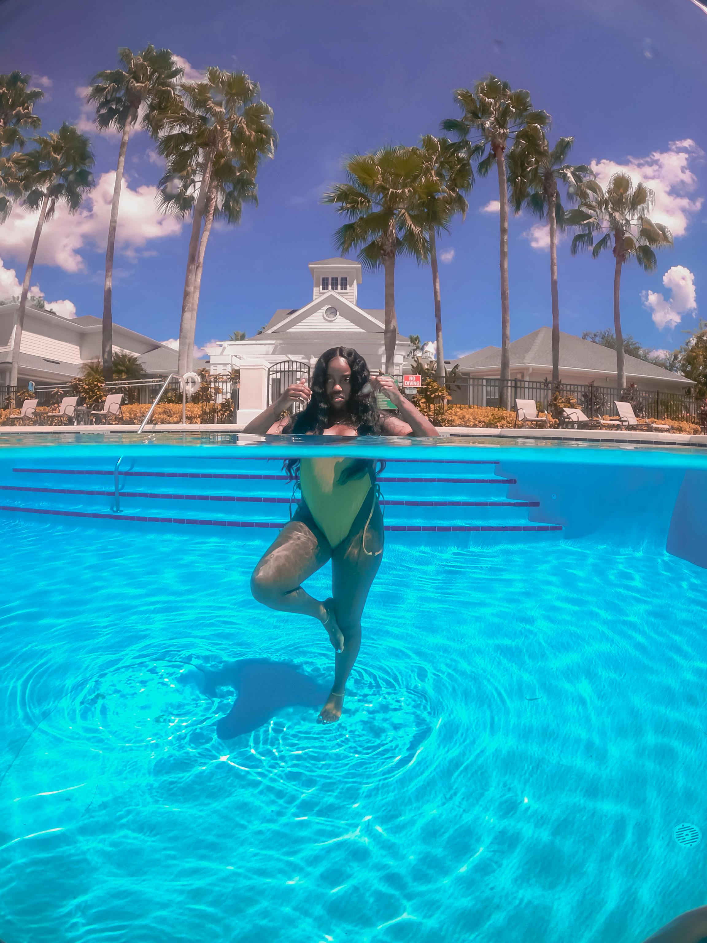 Free Elegant woman stands gracefully in a resort swimming pool under a clear blue sky, capturing the essence of summer vacation. Stock Photo