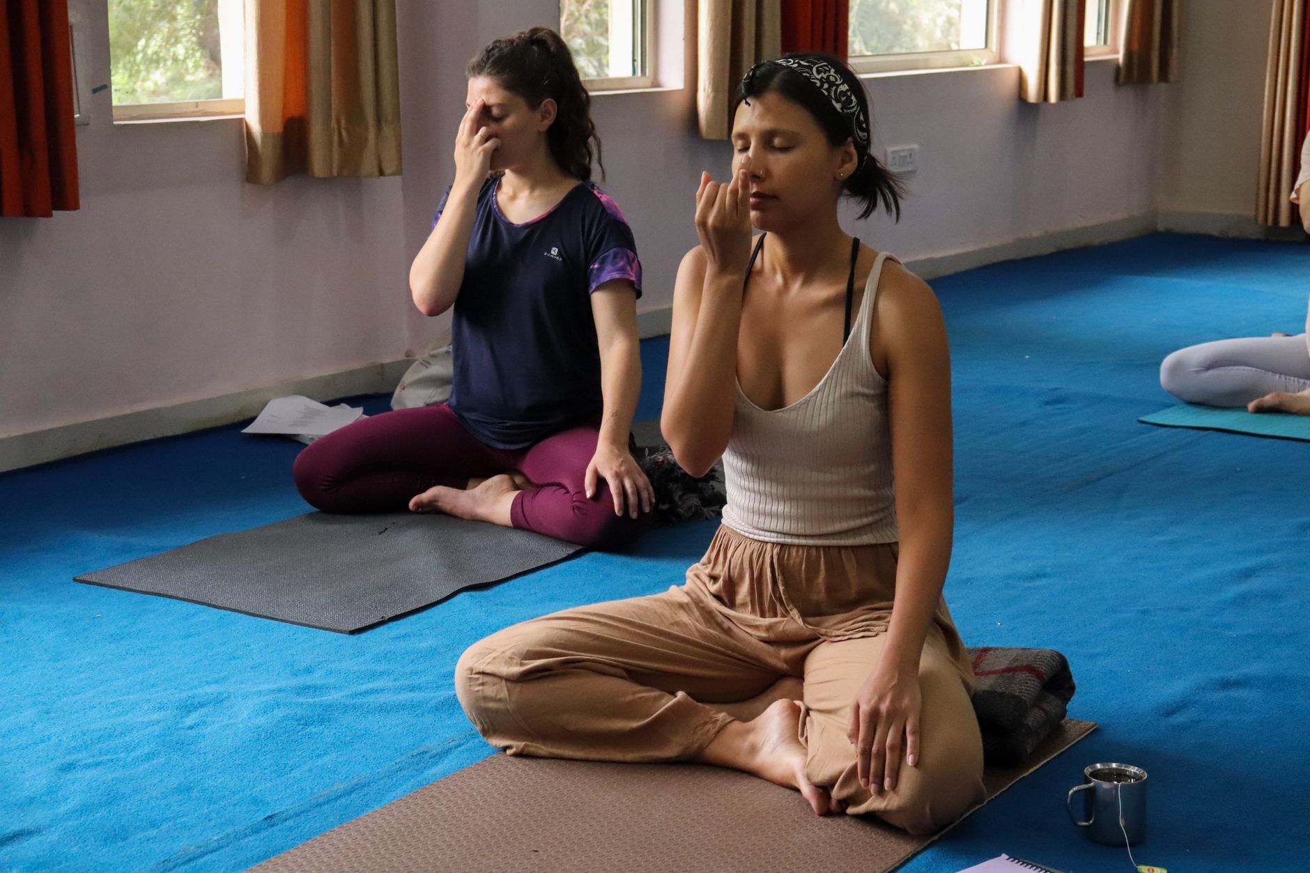Two women practicing yoga breathing exercises indoors in Rishikesh, India.