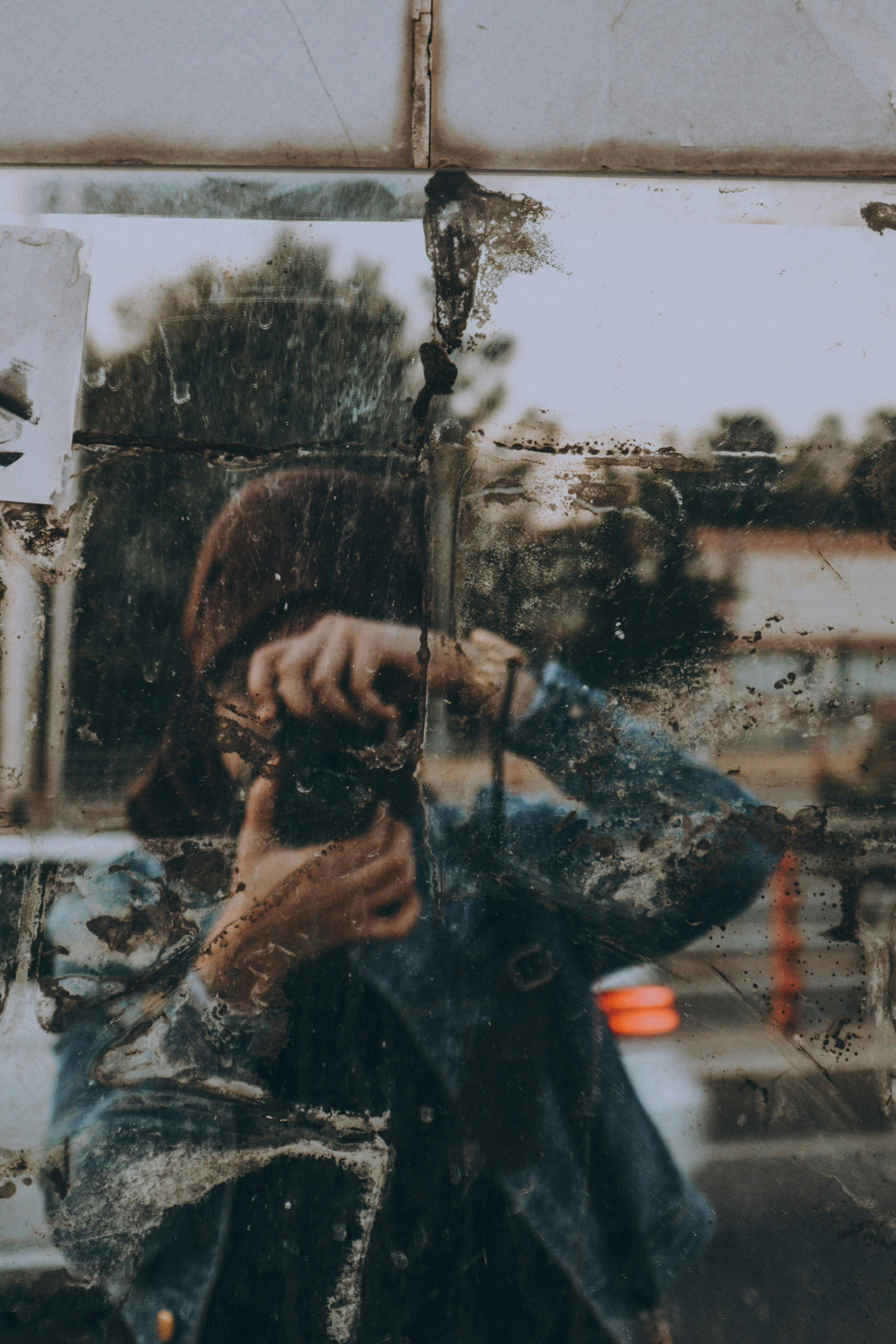 An artistic shot of a photographer's reflection in a grungy, aged mirror with a denim jacket.