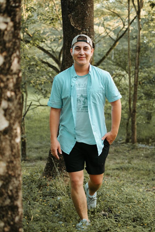 Man in Button Down Shirt Walking Beside the Trees