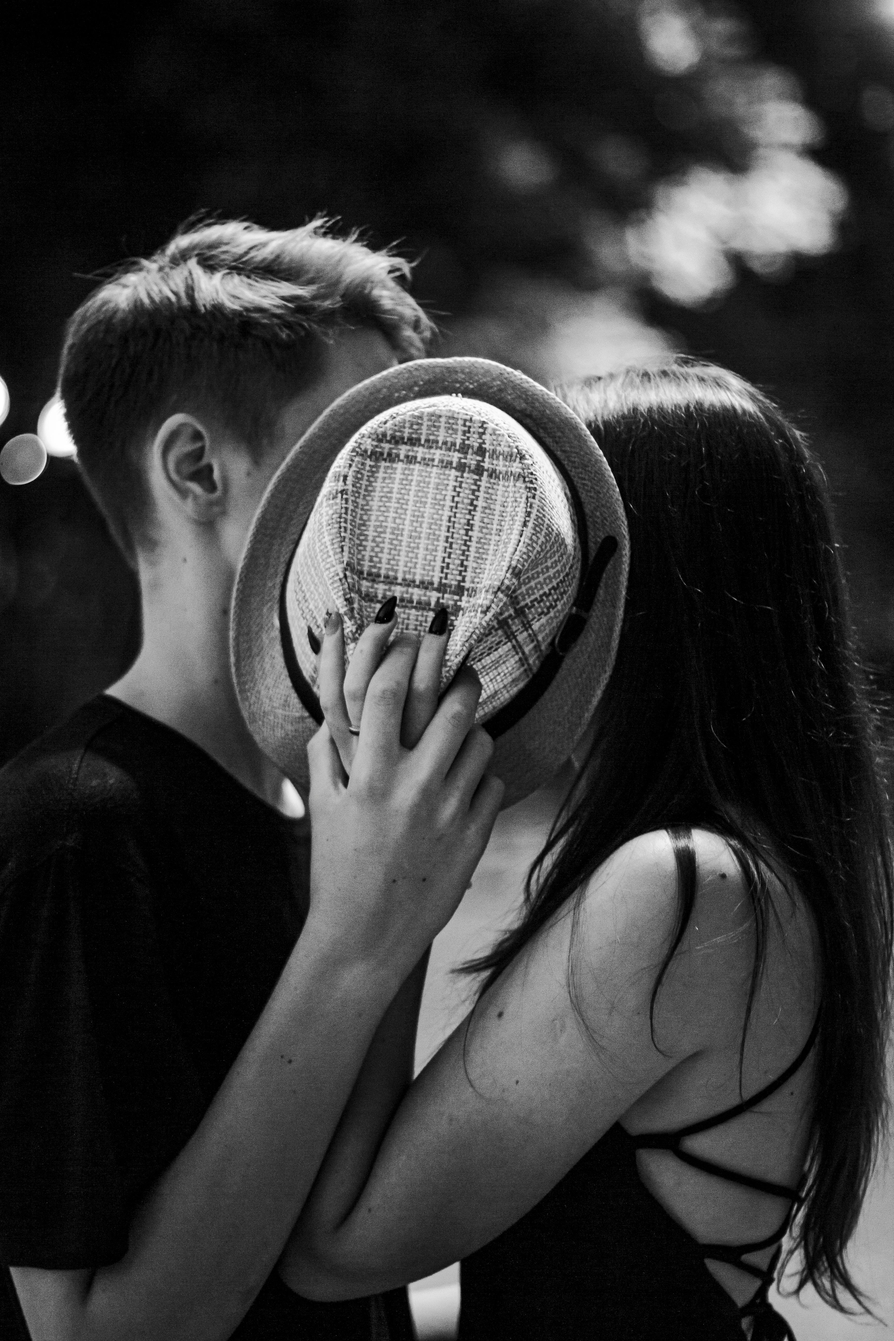 A young couple shares a moment of intimacy, hiding their faces behind a hat in this monochrome photo.