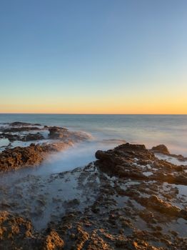A tranquil view of the sea and rocky shore during a calm sunset, perfect for nature lovers.
