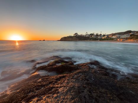 Stunning sunset view over a rocky shoreline with vibrant orange and blue hues.