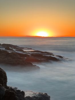 Stunning sunset over a rocky coastline with calm sea and vivid colors.