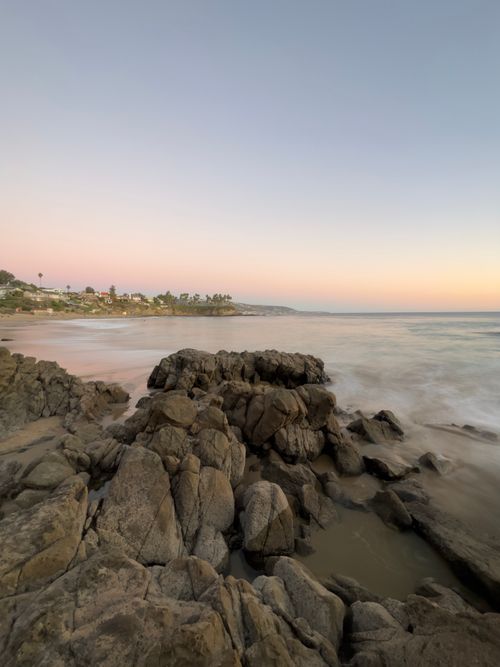 Free A serene view of a rocky coastline with pastel sunset hues creating a tranquil atmosphere. Stock Photo