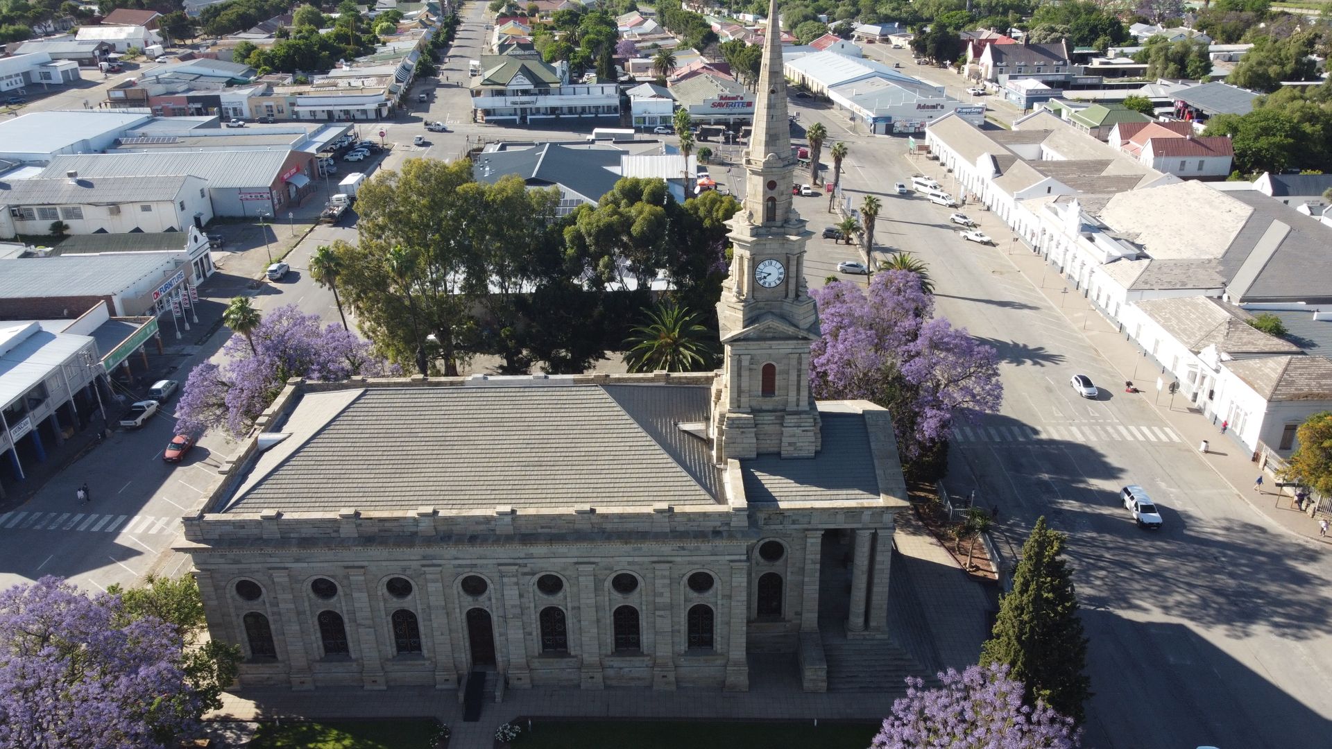 Aerial view of a historic church in Cradock, South Africa surrounded by jacaranda trees and city architecture.