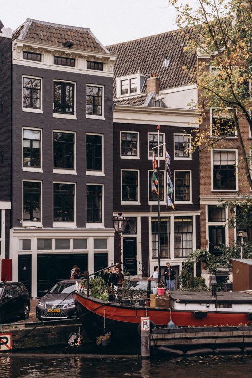 Free Picture of Amsterdam's iconic canal houses and a moored boat during the day. Stock Photo