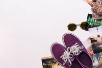 Purple canvas sneakers beside sunglasses and prints — photo by Diana on Pexels