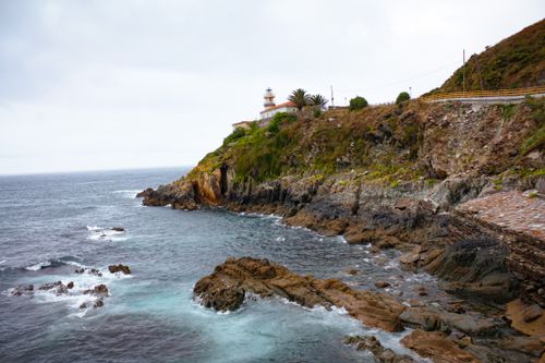 Free Dramatic view of a lighthouse on a rocky coastline with cloudy skies and ocean waves. Stock Photo