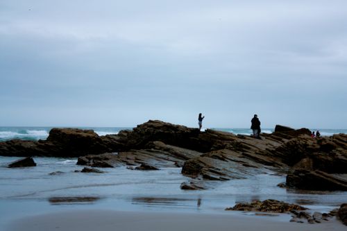 Free Two people silhouetted against rocky beach creating a serene and moody scene. Stock Photo