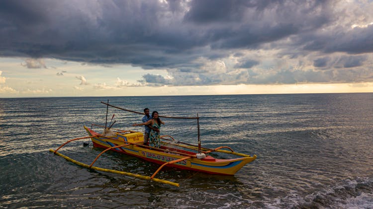 A Couple Standing On The Wooden Boat In The Water