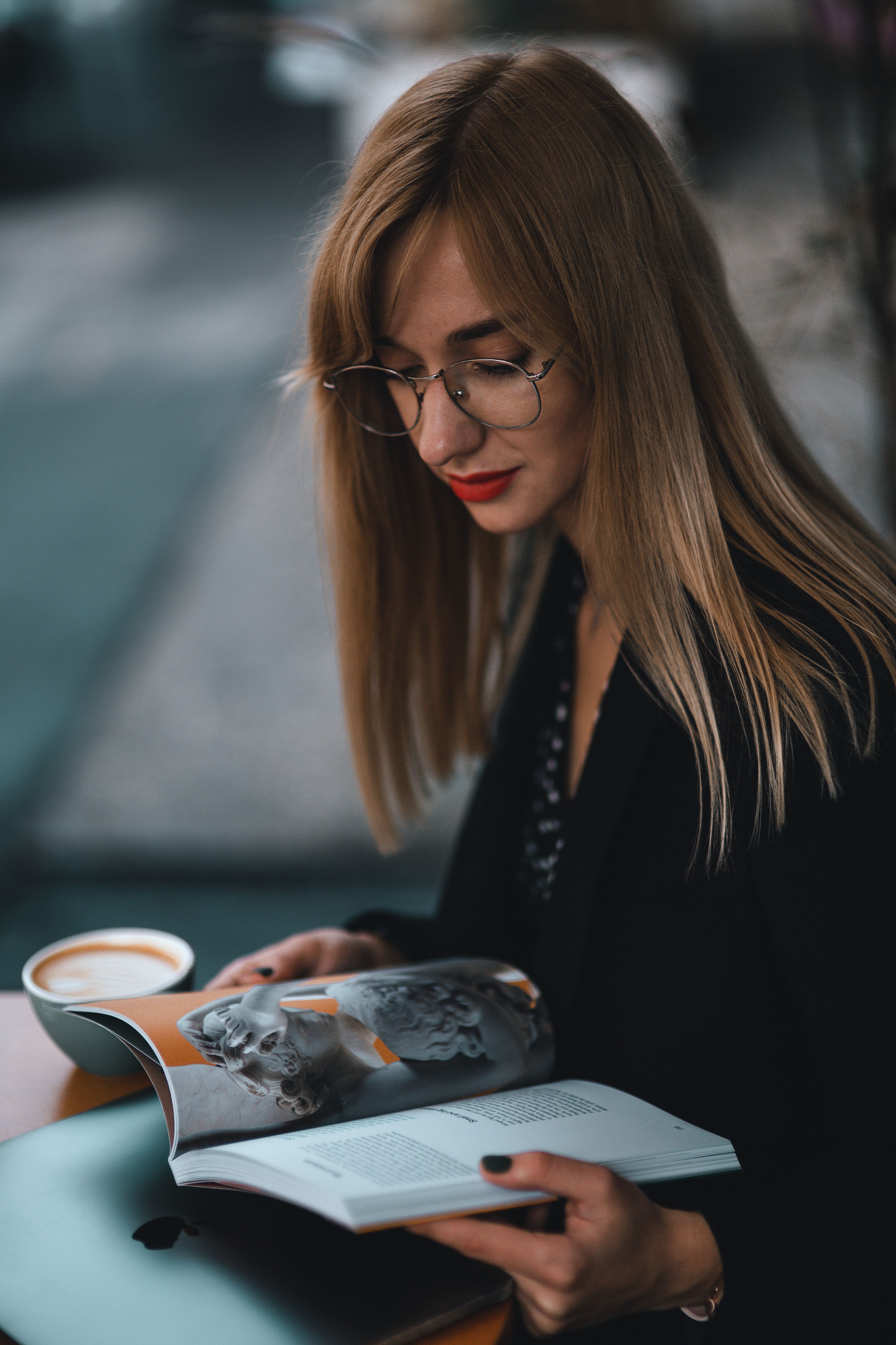 Thoughtful woman with eyeglasses reading a book indoors, enjoying coffee.