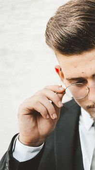 Close-up of a stylish man adjusting his eyeglasses, wearing formal attire. Ideal for fashion and lifestyle themes.