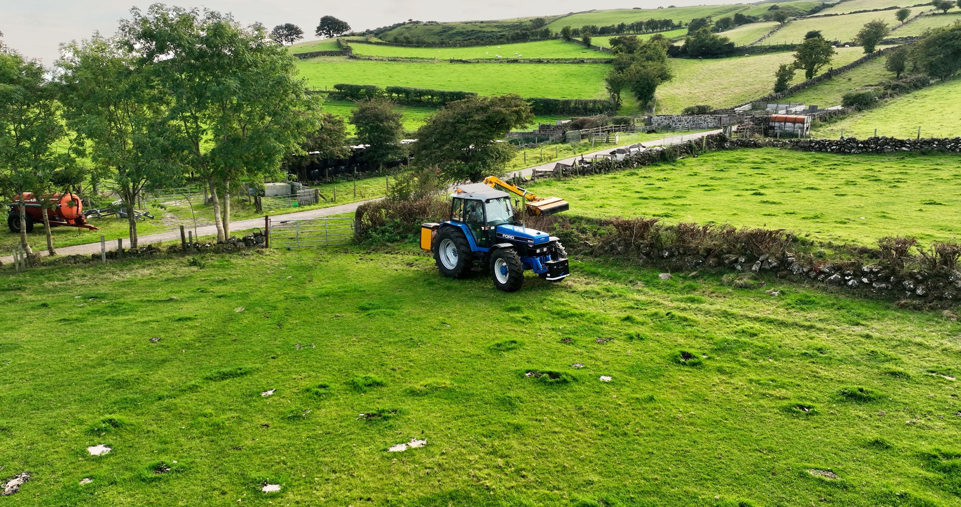 Aerial photo of a Blue New Holland Ford 8240 Tractor Cutting a hedge with a McConnel on farm in UK Co Antrim Northern Ireland 30-10-22